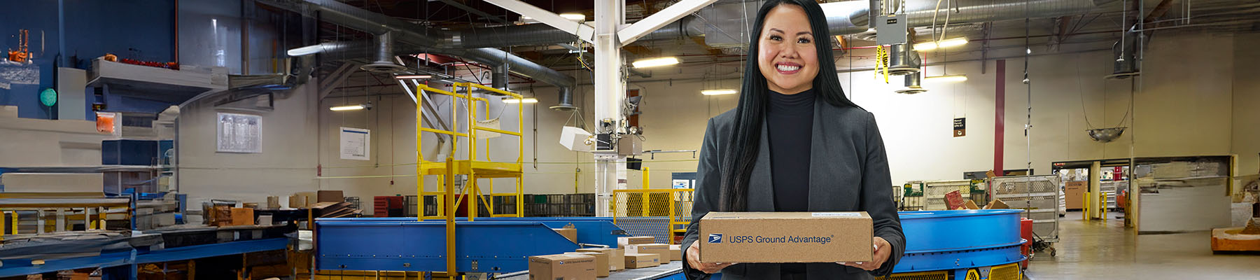 A person holding a USPS Ground Advantage package in a delivery center.